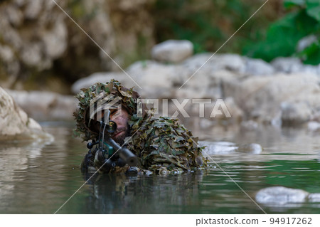 A military man or airsoft player in a camouflage suit sneaking the river and aims from a sniper rifle to the side or to target. A military man or airsoft player in a camouflage suit sneaking the river and aims from a sniper rifle to the side or to target. 94917262