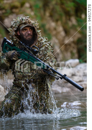 A military man or airsoft player in a camouflage suit sneaking the river and aims from a sniper rifle to the side or to target. A military man or airsoft player in a camouflage suit sneaking the river and aims from a sniper rifle to the side or to target. 94917278