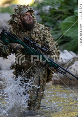 A military man or airsoft player in a camouflage suit sneaking the river and aims from a sniper rifle to the side or to target. A military man or airsoft player in a camouflage suit sneaking the river and aims from a sniper rifle to the side or to target. 94918123