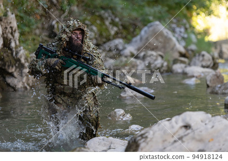 A military man or airsoft player in a camouflage suit sneaking the river and aims from a sniper rifle to the side or to target. A military man or airsoft player in a camouflage suit sneaking the river and aims from a sniper rifle to the side or to target. 94918124
