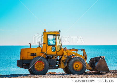Yellow bulldozer on the background of clear blue sky and sea. Copy space. Copy space and close up 94919430