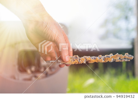 A man holding a anode damaged from corrosion. In the background the boiler and a view of the lawn. Close up. Light 94919432