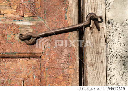 Shabby surface. Closed door. Rustic wooden texture. Grunge board gate with cracked surface of orange paint and metal hook copy space for text logo. 94919829