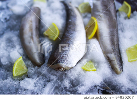 Fresh raw sea fish and lemon peces on ice surface. 94920207