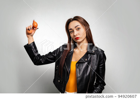 A young Caucasian woman in a leather jacket, holding chicken eggs in her hand. Gray background. Copy space. Feminism, girl power, and the concept of equal rights and independence for women A young Caucasian woman in a leather jacket, holding chicken eggs in her hand. Gray background. Copy space. Feminism, girl power, and the concept of equal rights and independence for women 94920607