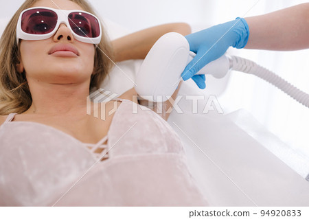 Beautician doing epilation on female's armpit in beauty center. Woman receiving laser light hair removal treatment for hairless smooth skin at cosmetology salon 94920833