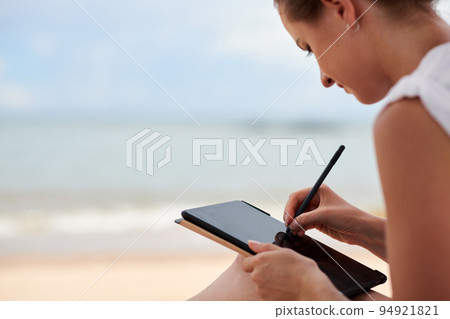 Young woman using digital tablet while sitting on the beach Young woman using digital tablet while sitting on the beach 94921821