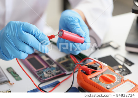 Hands hold a red lithium titanium battery and a voltmeter 94922724