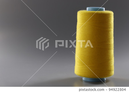 Big yellow bobbin of thin threads on a gray background Big yellow bobbin of thin threads on a gray background 94922804
