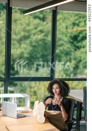 Cute brunette woman looking contented while sitting in the office and having coffee Cute brunette woman looking contented while sitting in the office and having coffee 94922953