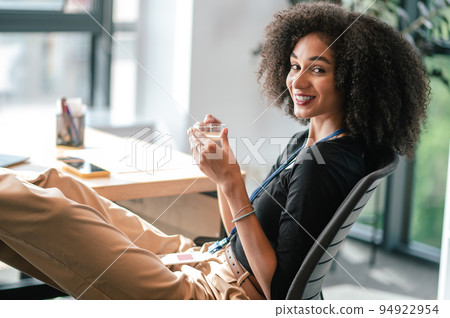 Cute brunette woman looking contented while sitting in the office and having coffee Cute brunette woman looking contented while sitting in the office and having coffee 94922954