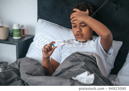 Sick boy lying in bed with fever and checking temperature 94923090