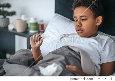 Sick boy lying in bed with fever and checking temperature 94923091