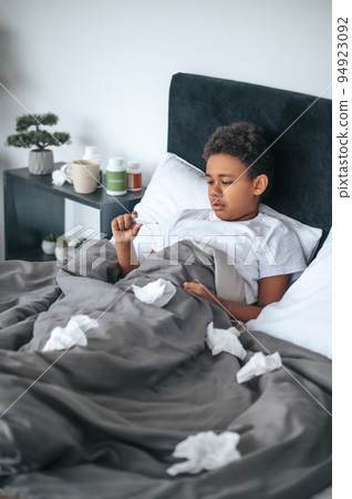 Sick boy lying in bed with fever and checking temperature 94923092