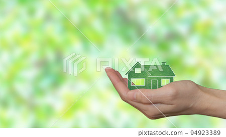 In the palm of a woman's hand, an eco-green house. Blurry green leaves in the background 94923389