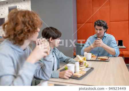 Male teacher and his pupils having lunch together Male teacher and his pupils having lunch together 94923449