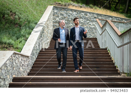 Two businessmen walking down the stairs and talking Two businessmen walking down the stairs and talking 94923483