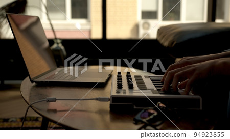 Woman hands playing on small midi controller, producer of music with laptop on table. Closeup of 94923855
