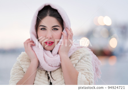 Winter portrait of happy brunette young woman on winter evening outdoors. Elegant young adult female with red plump lips, dressed in white fur coat and light pink scarf on head. Soft lighting twilight Winter portrait of happy brunette young woman on winter evening outdoors. Elegant young adult female with red plump lips, dressed in white fur coat and light pink scarf on head. Soft lighting twilight 94924721
