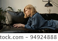 Young woman using laptop, chilling on a sofa in living room. Woman in jeans clothes concentrated 94924888