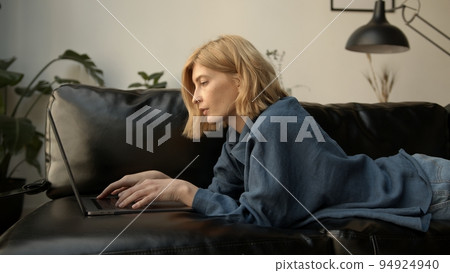 Young woman using laptop, chilling on a sofa in living room. Woman in jeans clothes concentrated 94924940