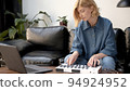 Woman playing on midi controller in living room with couch, producer of music with laptop on table 94924952