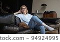 Blonde woman sitting on sofa with sleeping puppy. Woman telling a story, pet on the couch lying 94924995