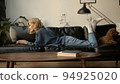 Young woman using laptop, chilling on a sofa in living room. Woman in jeans clothes concentrated 94925020