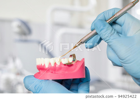 Dentist's hands with layout of the human jaw and dental restoration instrument. 94925422