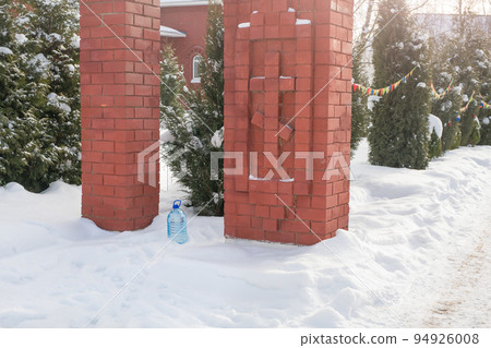 Orthodox Epiphany celebrations. Holy water is traditionally collected by people in the church on the day. A bottle of holy water in the snow on the background of the church Orthodox Epiphany celebrations. Holy water is traditionally collected by people in the church on the day. A bottle of holy water in the snow on the background of the church 94926008