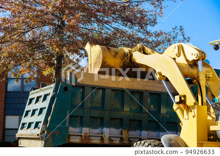 When the autumn season approaches, municipal workers remove fallen leaves from the ground near homes with a bulldozer and a truck When the autumn season approaches, municipal workers remove fallen leaves from the ground near homes with a bulldozer and a truck 94926633