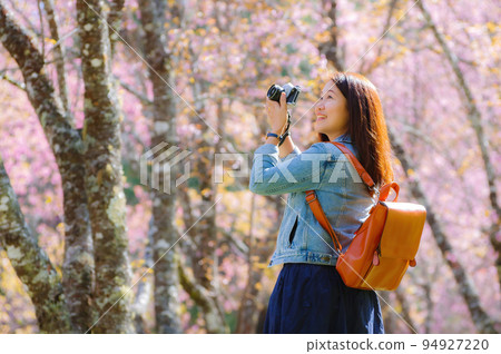 Beautiful Young Asian backpacker using vintage camera take a photo and smiling happiness in the midst of spring cherry blossoms bloom Travel lifestyle, world explorer, Asia travel idea. 94927220