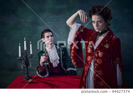 Portrait of man and woman in image of medieval vampires drinking blood at night over dark green background Portrait of man and woman in image of medieval vampires drinking blood at night over dark green background 94927374
