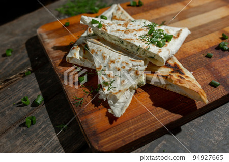 A dish of cottage cheese with parsley and onions in pita bread fried on a grate lie on a board A dish of cottage cheese with parsley and onions in pita bread fried on a grate lie on a board 94927665