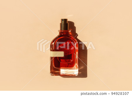 Transparent perfume bottle with red filling on a pastel beige background in the sunlight. Flat lay, top view. Luxury presentation mockup. Beautiful opened glass of aroma water 94928107