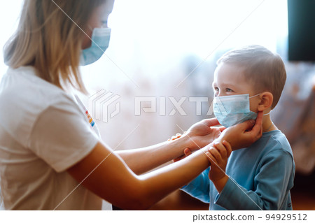 Little boy and mom in medical mask. Mother puts on her baby sterile mask. Child, wearing face mask. 94929512