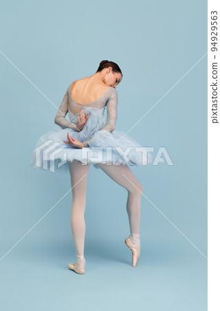 Portrait of tender young ballerina dancing, performing isolated over blue studio background. Delightful performance Portrait of tender young ballerina dancing, performing isolated over blue studio background. Delightful performance 94929563