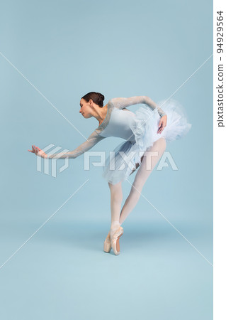 Portrait of tender young ballerina dancing, performing isolated over blue studio background. Delightful performance Portrait of tender young ballerina dancing, performing isolated over blue studio background. Delightful performance 94929564