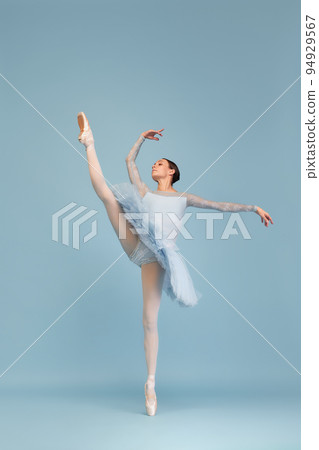 Portrait of tender young ballerina dancing, performing isolated over blue studio background. Standing on twine 94929567