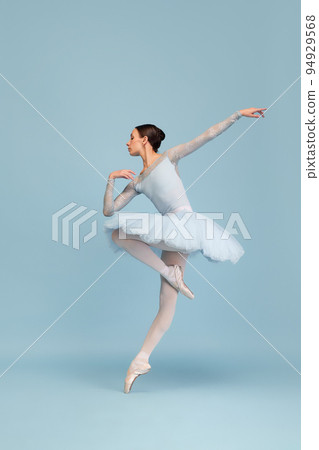 Portrait of tender young ballerina dancing, performing isolated over blue studio background. Tenderness, grace and elegance 94929568