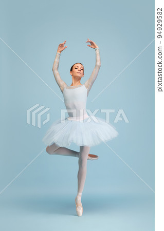 Portrait of tender, beautiful, young ballerina dancing, performing isolated over blue studio background. Femininity Portrait of tender, beautiful, young ballerina dancing, performing isolated over blue studio background. Femininity 94929582