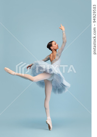 Portrait of tender young ballerina dancing, performing isolated over blue studio background. Standing on tiptoe 94929583