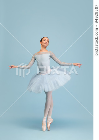 Portrait of tender young ballerina dancing, performing isolated over blue studio background. Beauty of classical dance 94929587