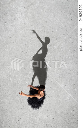 Portrait of young ballerina in black dress performing isolated over grey wall background. Top view. Shadow element. Classic dance 94929591