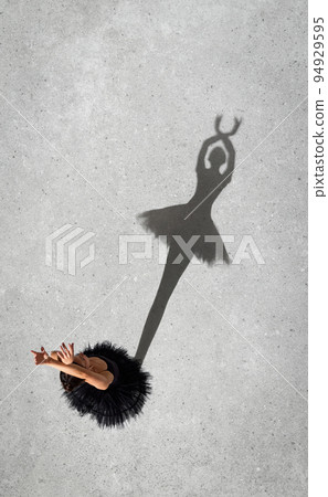 Portrait of young ballerina in black dress performing isolated over grey wall background. Top view. Shadow silhouette 94929595