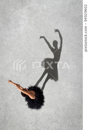 Portrait of young ballerina in black dress performing isolated over grey wall background. Top view. Shadow element. Tenderness Portrait of young ballerina in black dress performing isolated over grey wall background. Top view. Shadow element. Tenderness 94929602