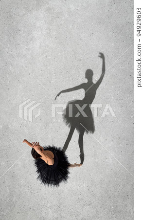Portrait of young ballerina in black dress performing isolated over grey wall background. Top view. Shadow element 94929603
