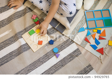 Confidence male kid in pajamas assembling geometric form shape on wooden board cells 94929765