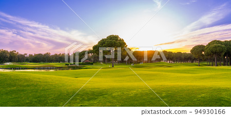 Golf course panorama at sunset with beautiful sky. Scenic panoramic view. Golf course with pine trees 94930166