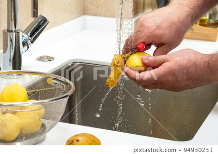 Close-up of male hands cooking potatoes with a potato peeler Close-up of male hands cooking potatoes with a potato peeler 94930231